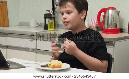 Kid eating eating homemade spaghetti and watching cartoon on tablet, Child boy having breakfast and playing game online on internet with friends before go to school in the morning.