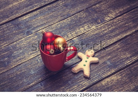 Cup of coffee and christmas balls and gingerbread man on wooden table.