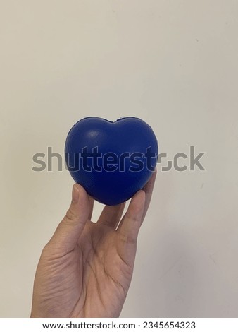 A heart-shaped blue ball photographed against a white wall.