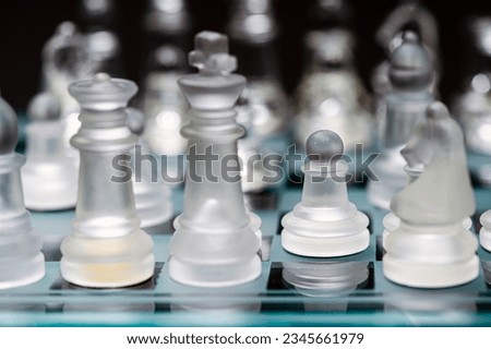 clear glass, transparent chess pieces on a checkerboard, selective focus, closeup, isolated on black