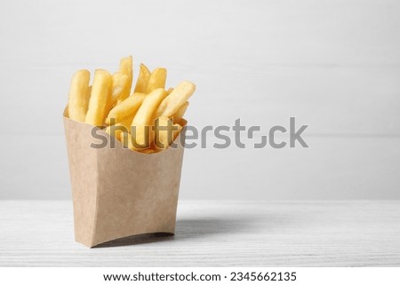 Delicious french fries in paper box on white wooden table, space for text Royalty-Free Stock Photo #2345662135