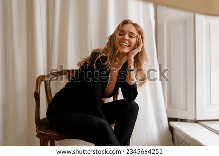 Chic and Elegant: Gorgeous Woman with Wavy Hair posing in stylish light appartments. Wearing  casual  black outfit.  Royalty-Free Stock Photo #2345664251
