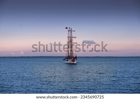 A three-master sails across the sea as dusk falls