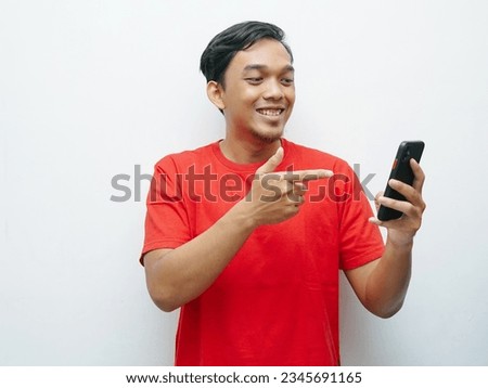 Portrait of young Asian Indonesian smiling while other hand finger pointing smartphone. Red t-shirt for 17 august indonesia independence day concept