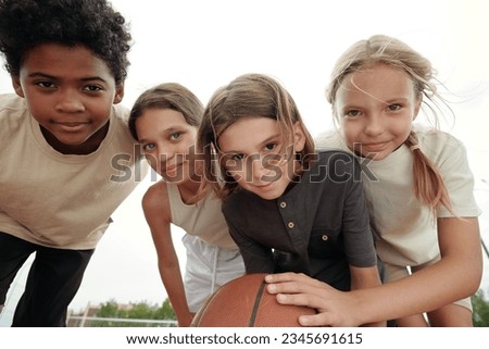 Four cute schoolkids in t-shirts and shorts bending forwards in front of camera and looking at you with smiles while blond boy holding ball