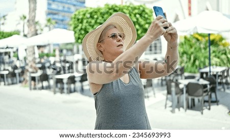 Middle age grey-haired woman tourist make photo by smartphone at coffee shop terrace