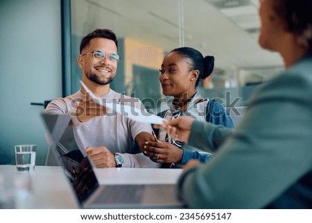 Happy man and his African American wife handing over paperwork to their bank manager in the office.  Royalty-Free Stock Photo #2345695147