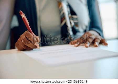 Close up of African American woman signing insurance agreement in the office. 