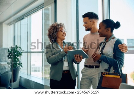 Happy financial advisor using touchpad while talking to young couple during the meeting. Copy space. Royalty-Free Stock Photo #2345695159