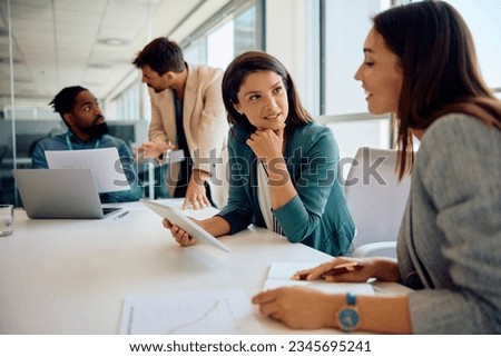 Mid adult businesswoman using digital tablet while talking to female coworker on a meeting in the office.  Royalty-Free Stock Photo #2345695241