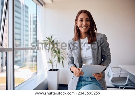Happy female entrepreneur working on digital tablet in the office and looking at camera. Royalty-Free Stock Photo #2345695259