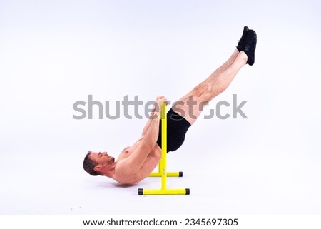 Young muscular man doing parallel bar exercises in dark white red studio with copy space