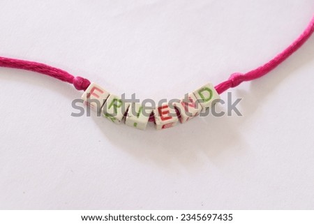A pink Friendship band made up of cubes and blocks with Friend written on it in different colours curved in a white isolated Background 