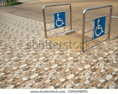 Ramp way for support wheelchair disabled people. Concrete ramp with stainless steel railing with blue handicapped sign installed on both the left and right of the ascent. 