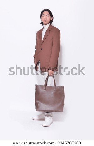 Full body portrait of handsome male wearing brown suit, khaki pants  holding handbag posing on white background