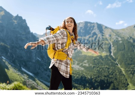 Young beautiful tourist woman with curly hair on top of a mountain. Active woman enjoys the beautiful scenery of the majestic mountains. Travel, adventure. Concept of an active lifestyle. Royalty-Free Stock Photo #2345710363