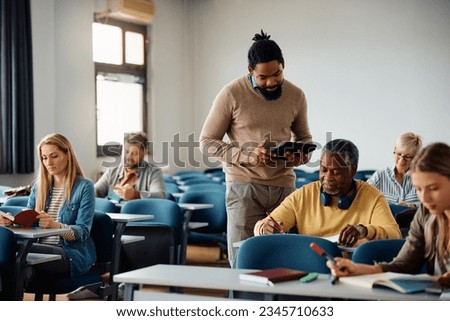 African American professor assisting his adult students during education class in the classroom. Royalty-Free Stock Photo #2345710633