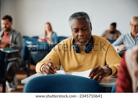 Smiling African American senior man taking notes while attending educational course in the classroom. Royalty-Free Stock Photo #2345710641