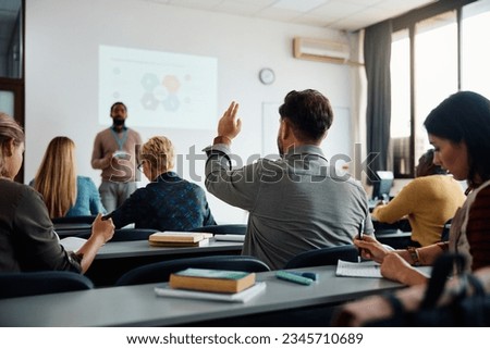 Rear view of man raising arm to ask a question during a presentation in lecture hall.  Royalty-Free Stock Photo #2345710689