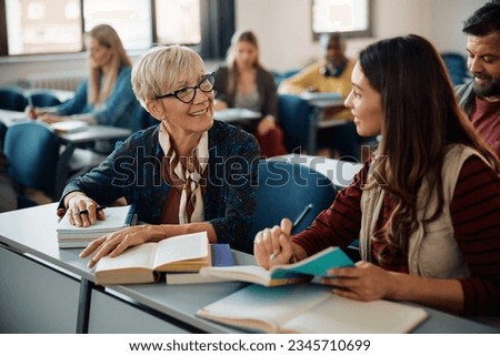 Smiling female adult learners communicating during a class in lecture hall. Focus is on mature woman.  Royalty-Free Stock Photo #2345710699