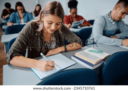Happy female student taking notes during a class in lecture hall. 