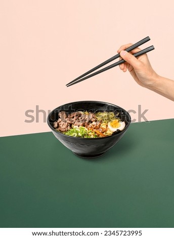 Photo of Japanese ramen soup with chopsticks and hand on the background. The perfect picture for a poster. Modern food concept. Advertising for a restaurant. The image is fully sharp, front to back.