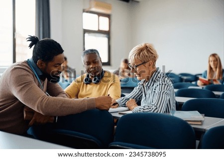 African American adult education teacher assisting his students during a course in the classroom. Focus is on mature woman.  Royalty-Free Stock Photo #2345738095