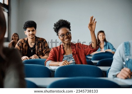 Happy African American college student raising her arm to answer the question during a lecture in the classroom. 
