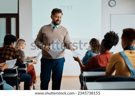 Happy teacher handing over test results to his students in the classroom.  Royalty-Free Stock Photo #2345738155