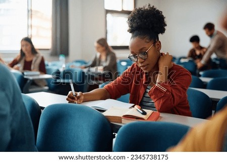 African American university student writing in her notebook while studying in the classroom.