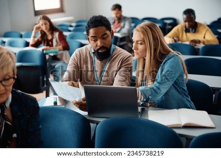 Mid adult woman learning with help of African American teacher during educational course in the classroom. Royalty-Free Stock Photo #2345738219