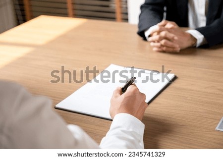 Businessman sitting at desk signing resignation letter and showing to boss or manager for approval signature to leave work, man quitting job or being fired from company. Royalty-Free Stock Photo #2345741329