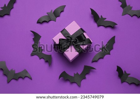 Composition with gift box and paper bats for Halloween on purple background
