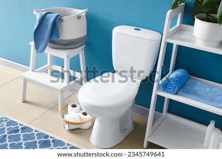 Interior of modern restroom with ceramic toilet bowl and shelving unit near blue wall Royalty-Free Stock Photo #2345749641