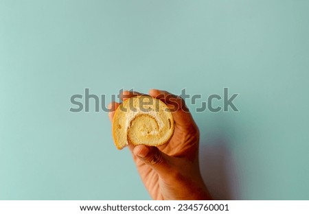Young asian women pick mini vanilla roll cake, swiss roll cake or sponge roll with Vanilla flavor. Thai call Jam Rolls. isolated on blue background Royalty-Free Stock Photo #2345760001
