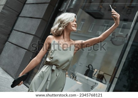 Fashion. Young stylish woman walking on the city street taking selfie photo on smartphone smiling cheerful