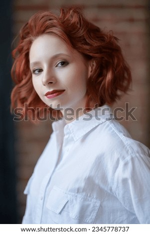 Portrait of a beautiful happy girl with curly ginger hair smiling and looking at the camera and smiling dreamily. Happy people, life pictures, emotions.