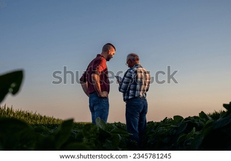 Two farmers standing in a field examining soy crop while using tablet.