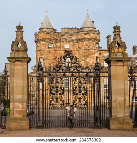 An eager tourist takes pictures from the closed main gates of the Palace of Holyroodhouse, located at the East end of The Royal Mile in Edinburgh, Scotland
