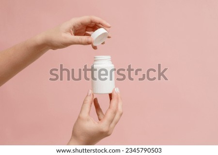 White bottle (plastic tube) in hand on a pink background. Packaging for vitamins, pill or capsule, or supplement. Mockup for product branding Royalty-Free Stock Photo #2345790503