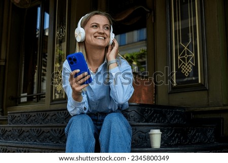 Smiling young woman with headphones and smartphone sitting on steps