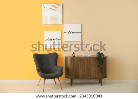 Grey armchair and wooden cabinet near colorful wall with different paintings