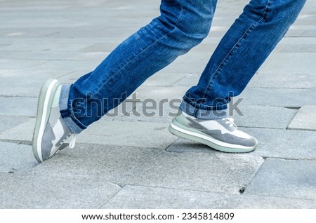 close-up of a woman's feet in jeans and sneakers tripping over unevenly laid paving slabs. Accident, injury on a walk due to poor road surface. Royalty-Free Stock Photo #2345814809