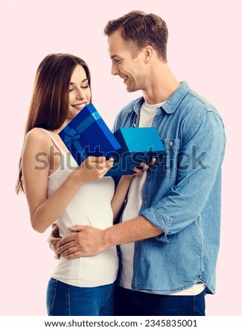 Portrait photo - happy smiling young couple opening blue gift box, isolated over rose pink background. Caucasian models in Valentine holiday sales offers ad concept.