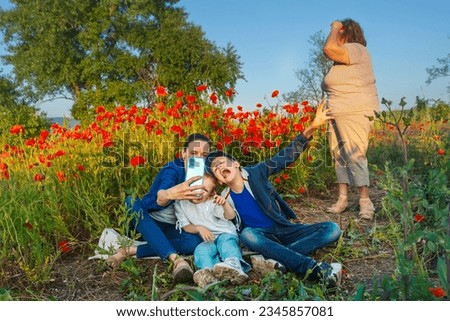 Mom and children take pictures of themselves on the phone, making funny faces in a poppy field on a summer day, grandmother turned