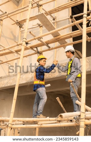 Two Asian male engineers shaking hands and working together Hope stands on the architectural construction site on the structure industry. Wear a helmet with a checkered shirt.