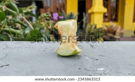 A green apple nibbled on a concrete fence in a garden with copy space. Bitten apple. 