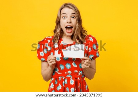 Young excited shocked fun caucasian woman she wear red dress casual clothes hold gift certificate coupon voucher card for store isolated on plain yellow background studio portrait. Lifestyle concept