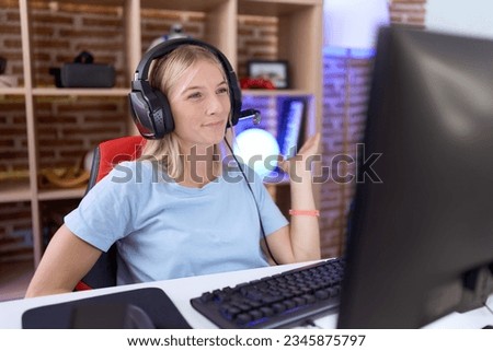 Young caucasian woman playing video games wearing headphones smiling cheerful presenting and pointing with palm of hand looking at the camera. 