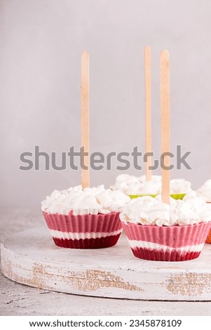 Strawberry ice cream popsicle lollies with whipped cream frozen in muffin molds on gray background. 